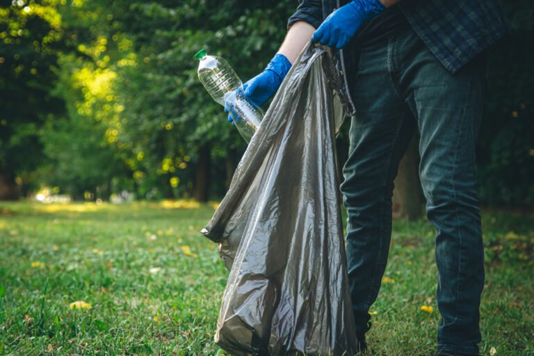 a man cleans up the forest, throws a bottle into a trash bag, close up.
